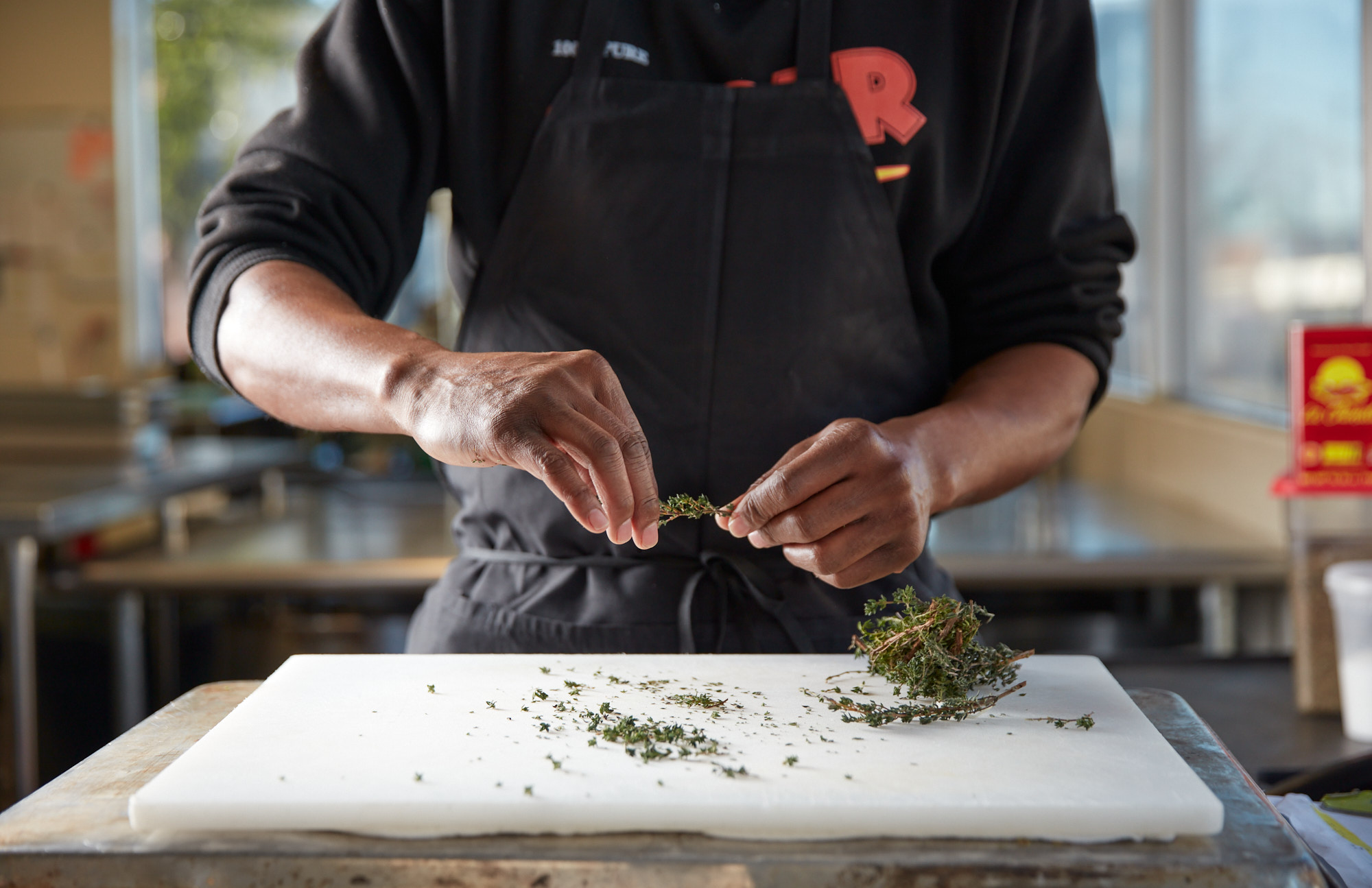 A Just Fare chef in a black apron stripping fresh thyme leaves onto a white cutting board