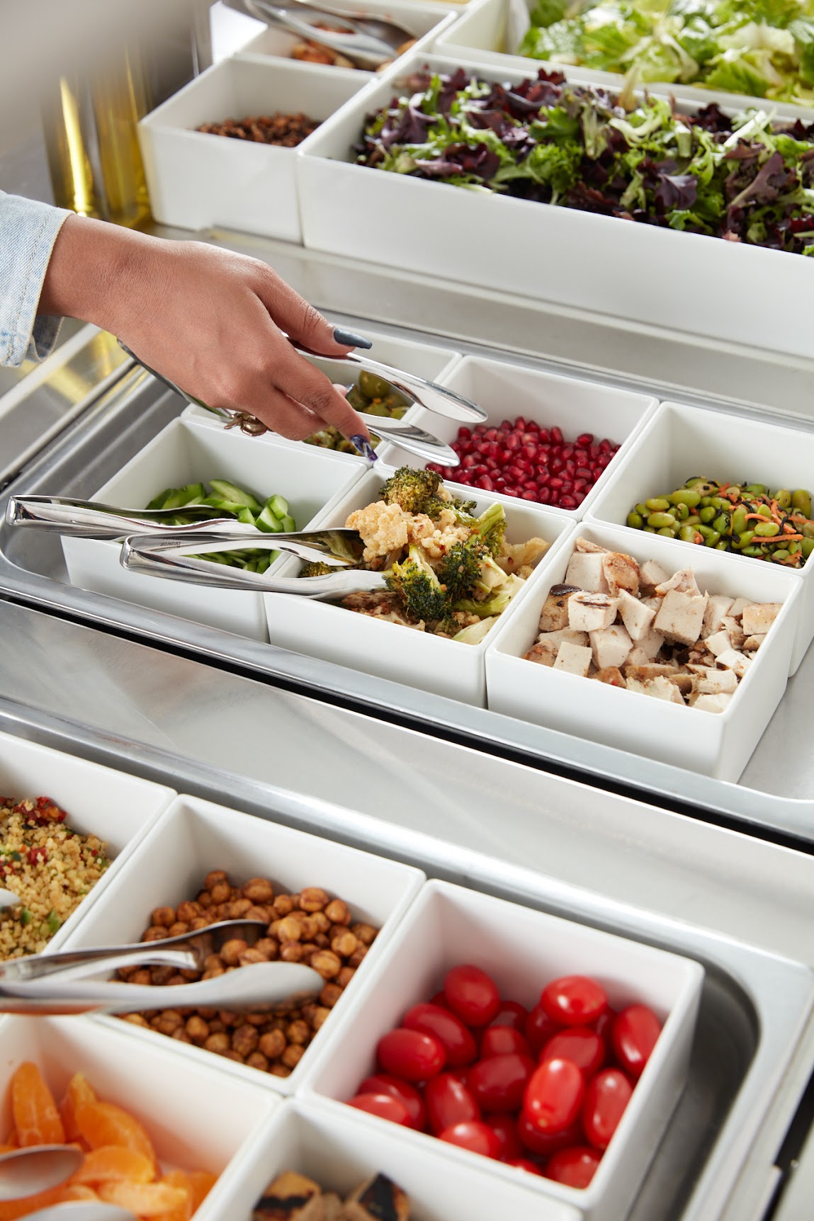 Just Fare salad bar with white porcelain inserts filled with greens, pomegranate, grilled chicken, edamame, cherry tomatoes, chickpeas, and grain salad